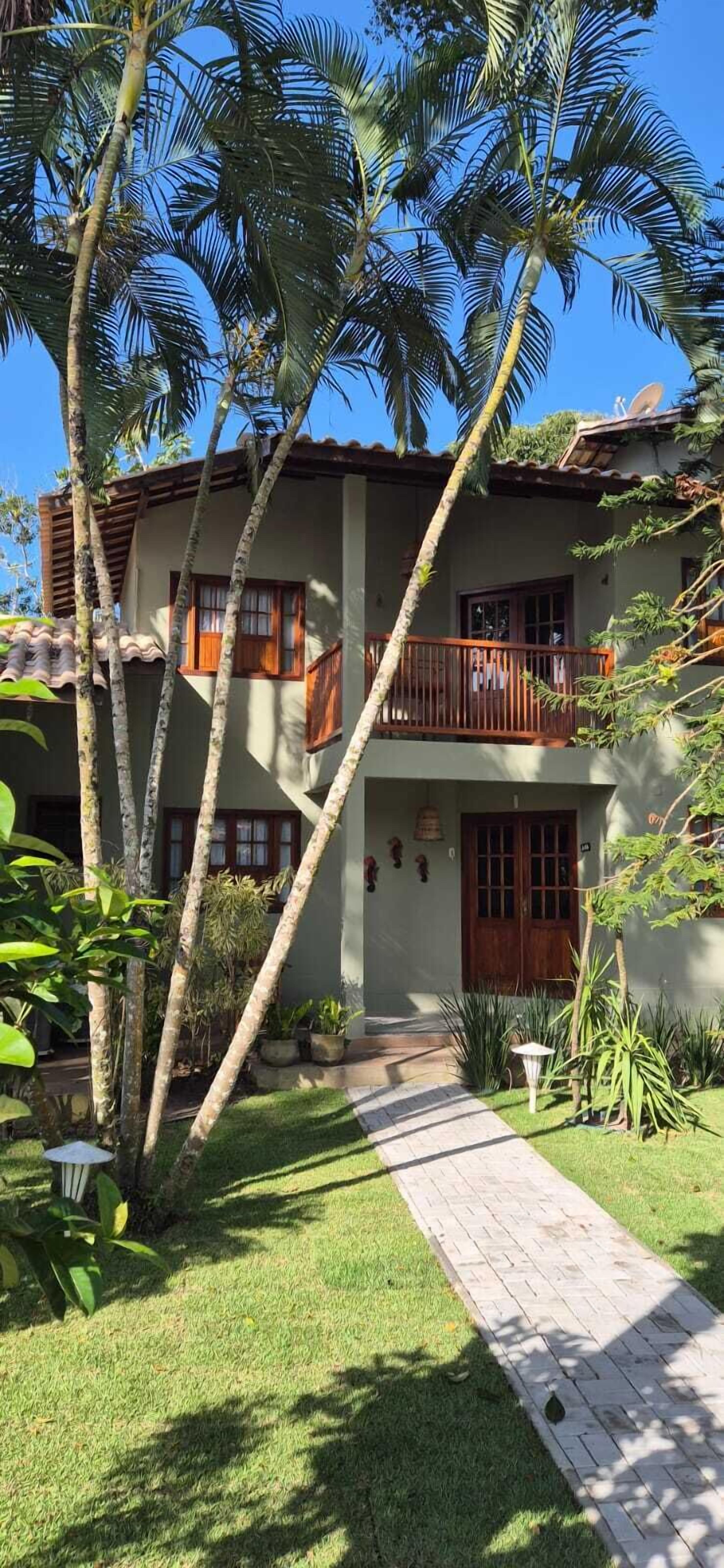 A two-story building with a balcony, surrounded by palm trees and a paved pathway.
