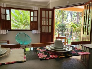 Ein Zimmer mit Holztisch, einem Stuhl und Blick auf einen üppigen Garten durch offene Türen.