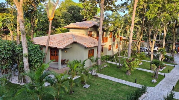 A two-story house with a tiled roof, surrounded by a well-maintained garden with palm trees and a paved walkway. - Residencial Maria Pitanga (Porto Seguro)