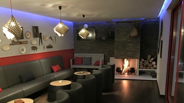 Een moderne zithoek met een bank, ronde tafels en hanglampen. Achterin is een open haard met hout zichtbaar.