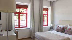 Een hotelkamer met een bed, een bureau, twee ramen met rode kaders en een lamp.