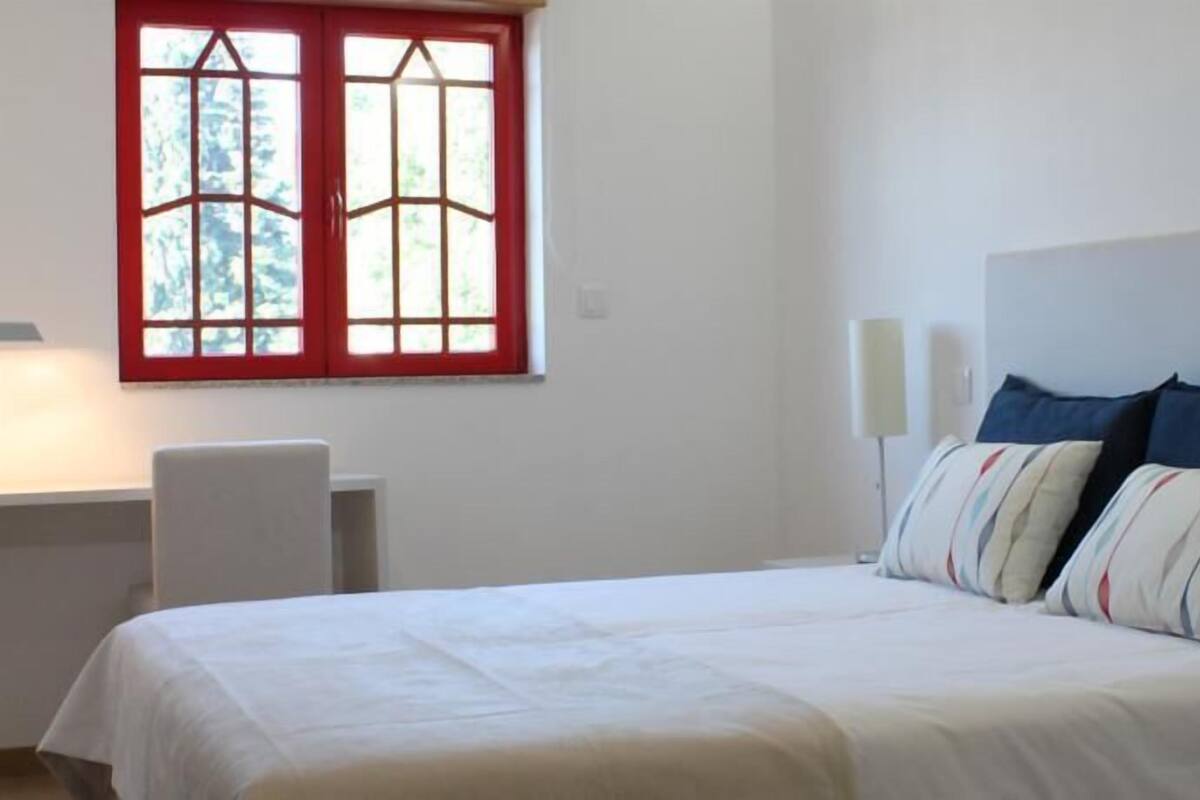 Une chambre à coucher avec un lit, un bureau et une fenêtre aux montants rouges.