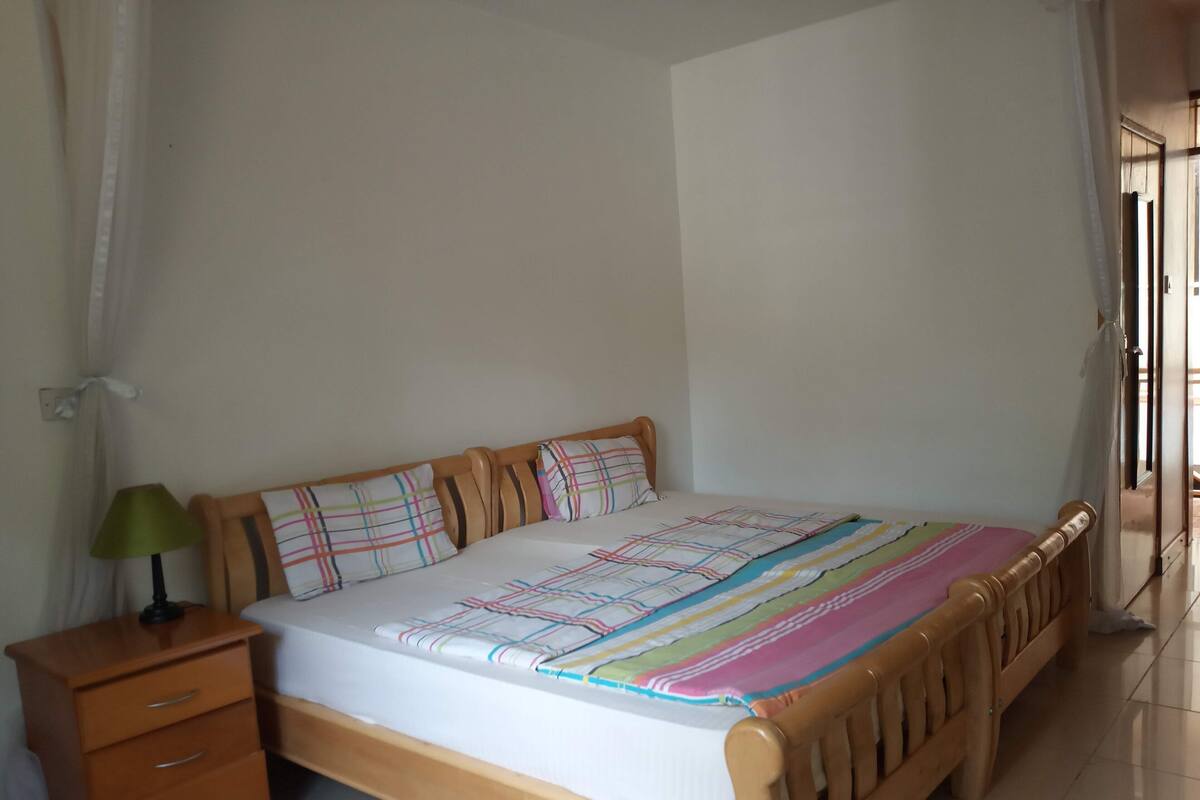 A single-bed room with a wooden headboard, a bedside table with a lamp, and a striped blanket.