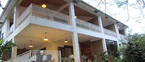 A two-story building with a balcony on the upper floor, potted plants, and a staircase leading to the entrance.