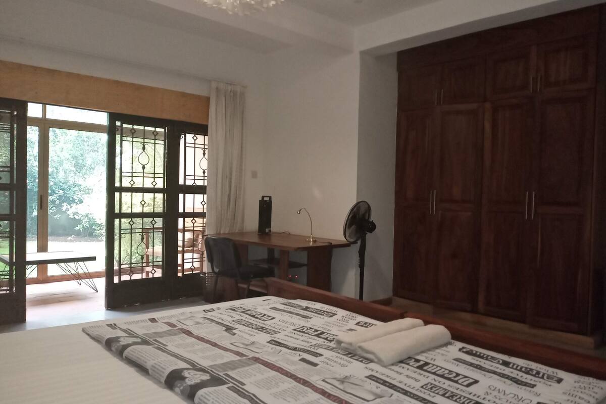 A room with a bed, a desk, a chair, a fan, and a wardrobe.