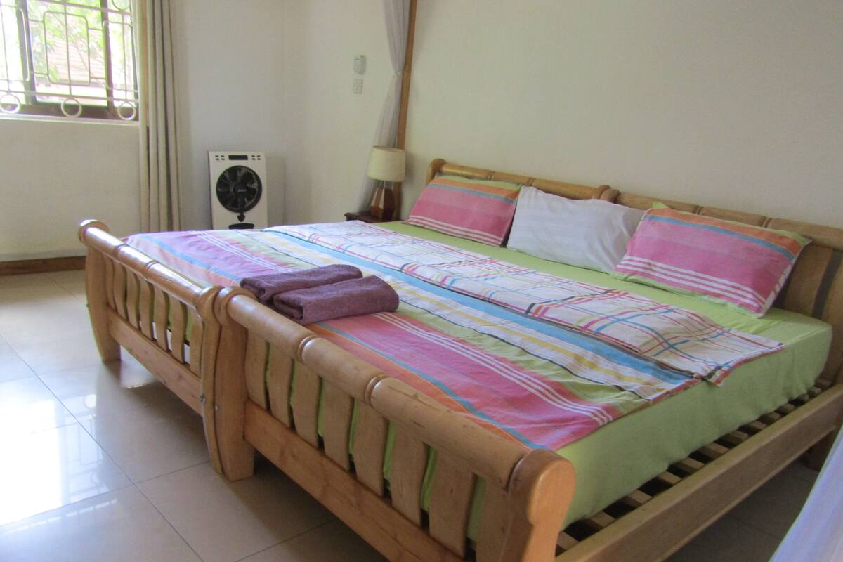 A wooden bed with a colorful bedspread, two pillows, and two folded towels.