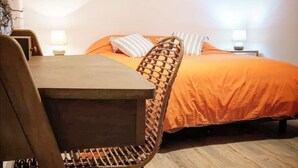 A room with a wooden table and chair, a bed with orange bedding, and two bedside lamps.