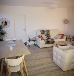 A modern living room with a wooden dining table, white sofa, and a small side table.