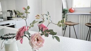 A kitchen with white cabinets, a white countertop, and a vase with pink flowers.