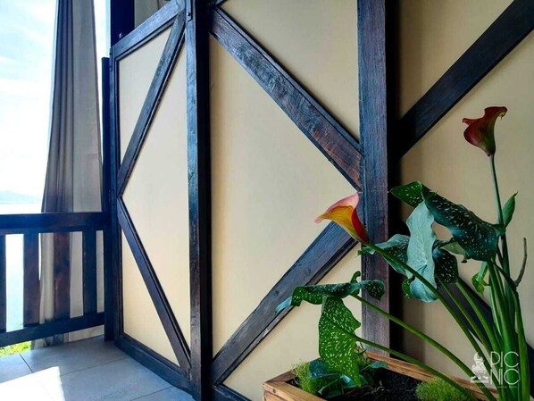 A balcony with a wooden railing, a potted plant with green leaves and a red flower, and a wall with a geometric pattern. - El Picnic Atitlan (Santa Cruz La Laguna)
