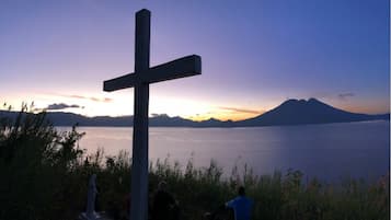 Una cruz con vistas a montañas y un cuerpo de agua al atardecer.