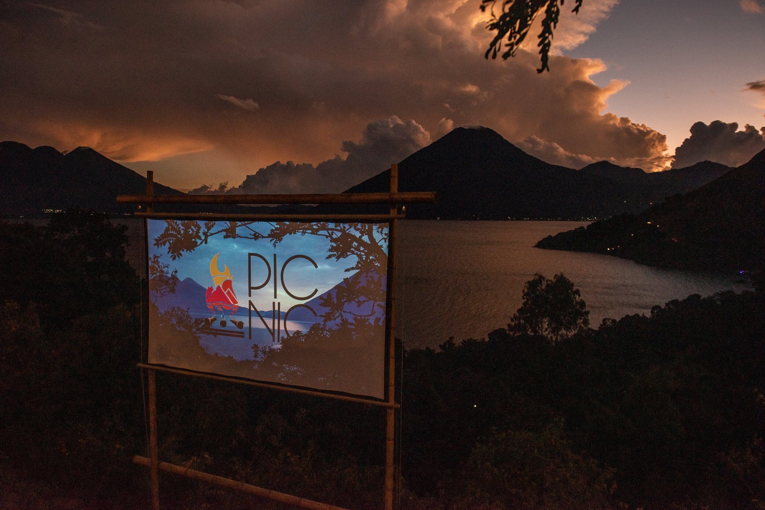 Ein Schild mit der Aufschrift 'PICNIC' vor Bergelandschaft und See im Abenddämmerung.