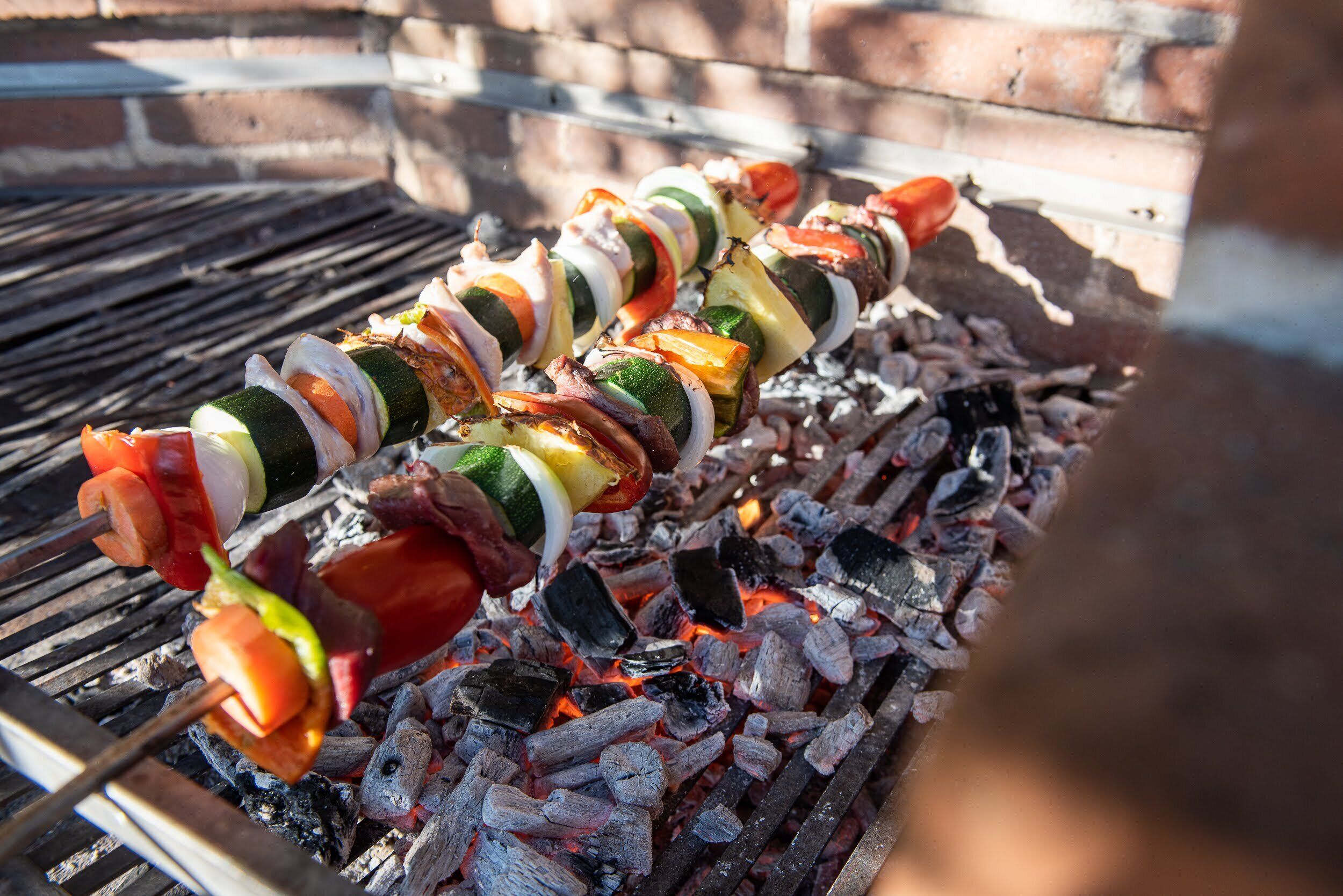 Una parrilla con brochetas de carne y vegetales cocinándose sobre carbón.
