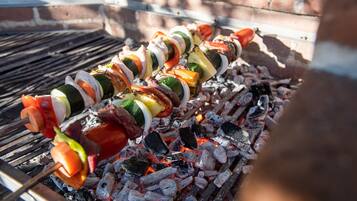 Una parrilla con brochetas de carne y vegetales cocinándose sobre carbón.