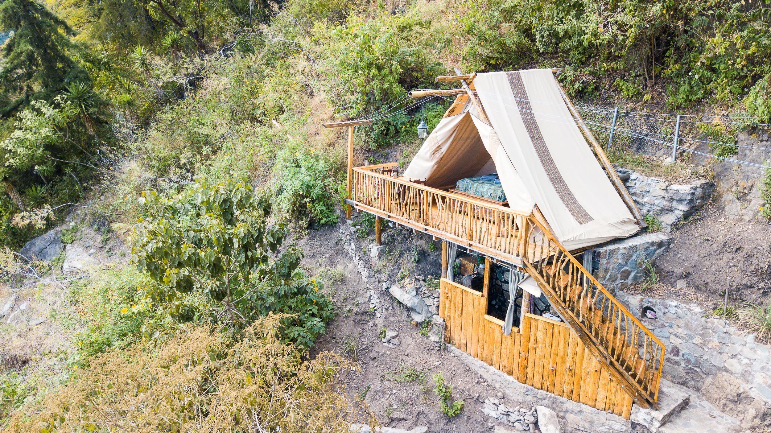 Une cabane en bois, dotée d’un toit en pente, entourée d’un terrain rocheux et d’une végétation dense.