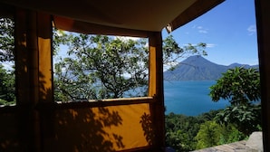 A window with a view of a lake, trees, and a mountain. - El Picnic Atitlan (Santa Cruz La Laguna)