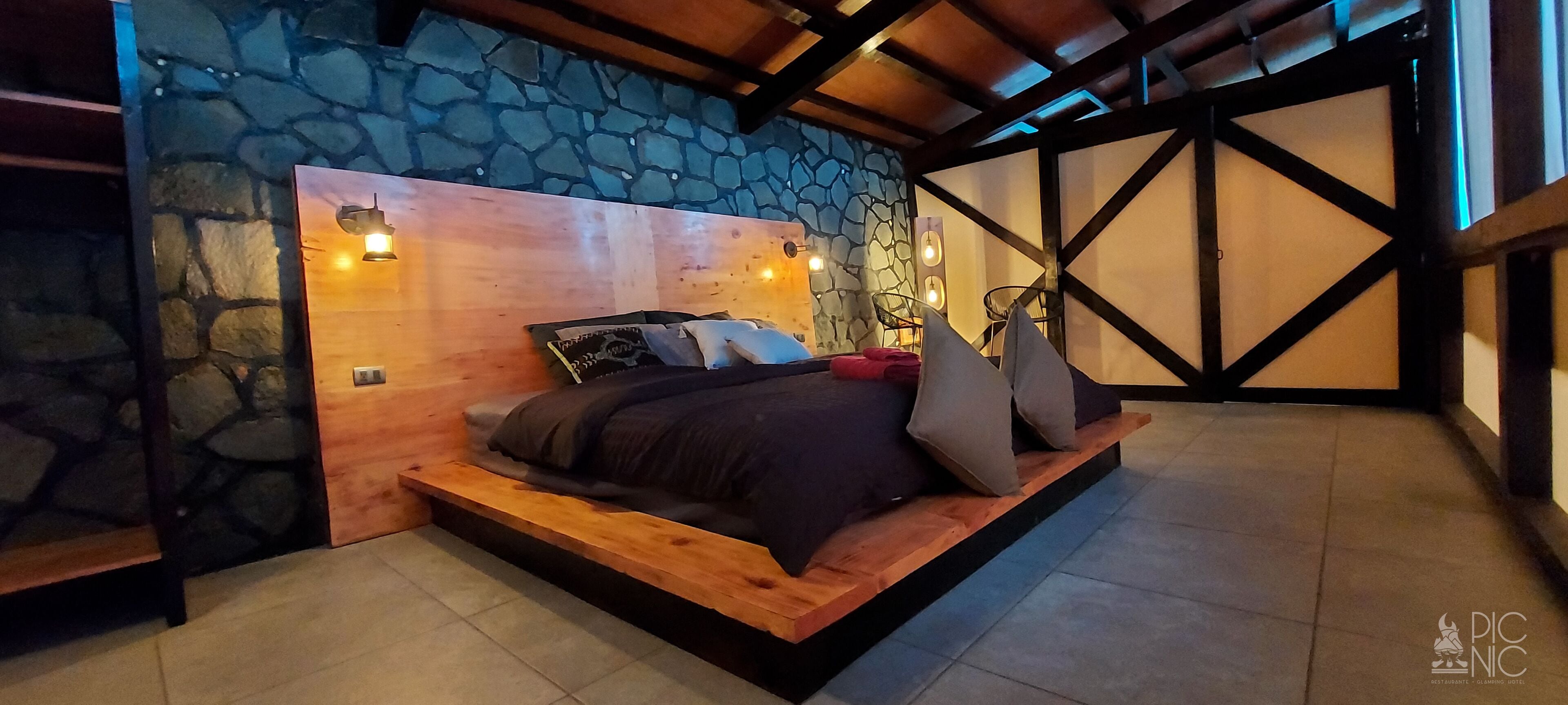 Une chambre avec un mur en pierre, une tête de lit en bois et un lit avec des oreillers.