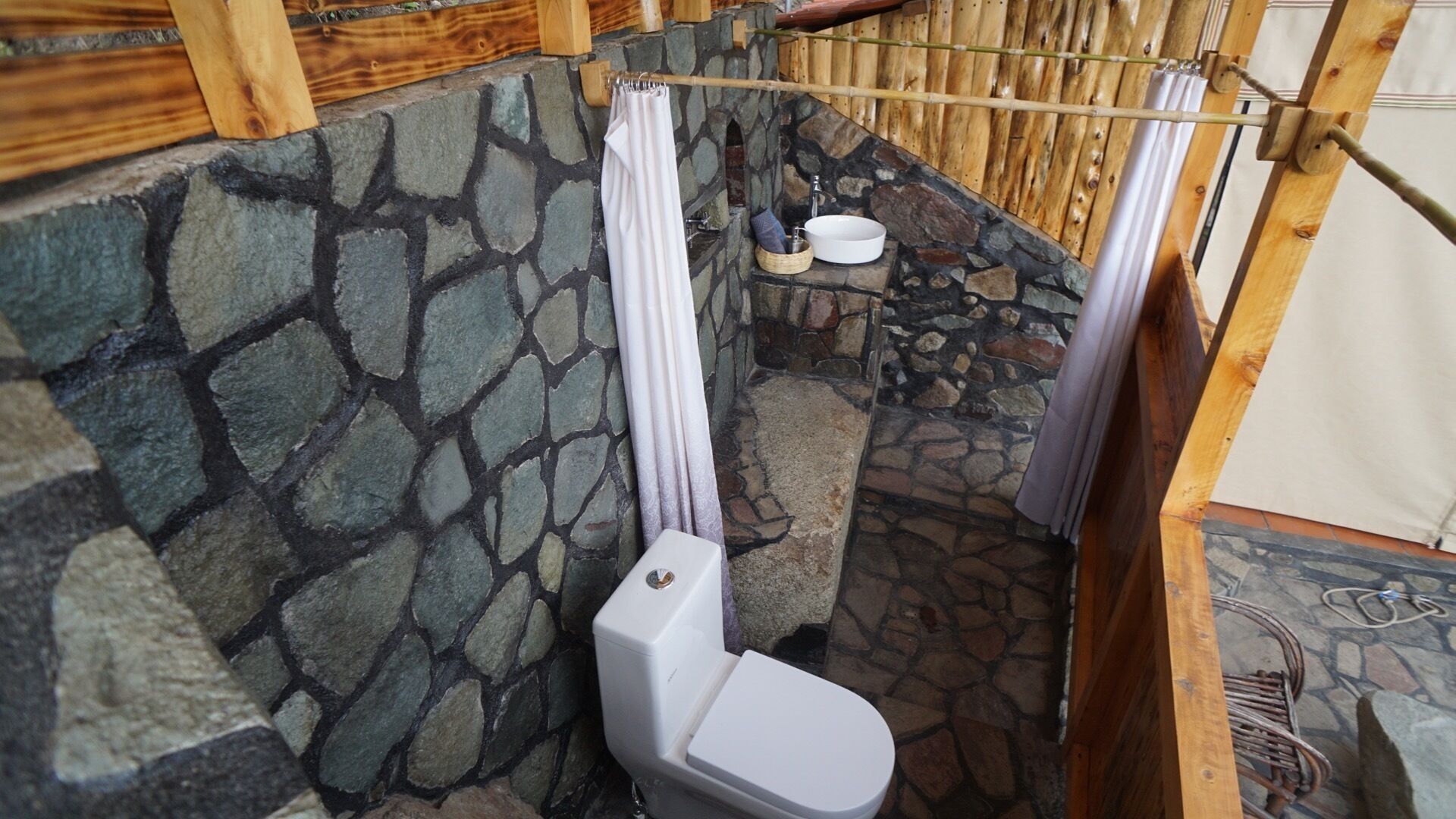 Baño con paredes de piedra, inodoro, lavabo y cortina de ducha.