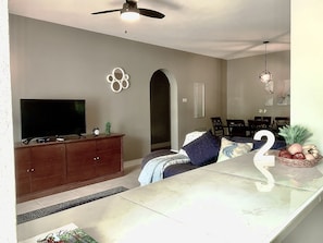 A modern living room with a flat-screen TV, wooden cabinet, and a dining area with a table and chairs.