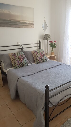 A bedroom with a bed, a nightstand, a lamp, a vase with flowers, and a painting on the wall.
