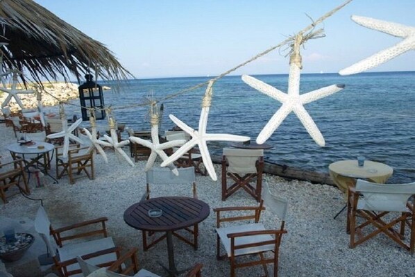 A beachside outdoor seating area with tables and chairs, starfish decorations, and a thatched umbrella.
