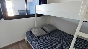 Dormitorio con literas, ventana, suelo de madera y colcha estampada.