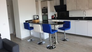 Una cocina moderna con encimera negra, armarios blancos y campana extractora negra. Hay cuatro taburetes azules alrededor de una mesa redonda.