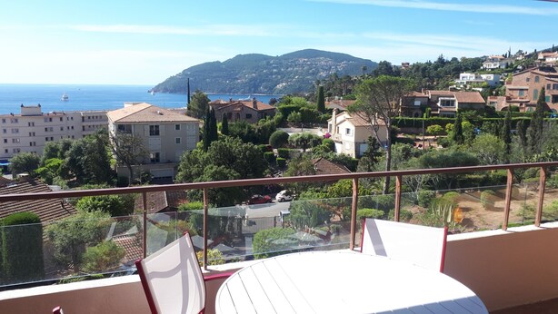 Un balcón con vista despejada a un pueblo costero, que incluye edificios, árboles y el mar.