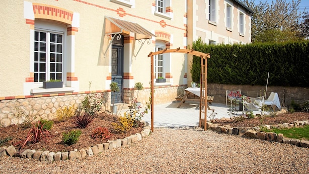 Une maison à deux étages avec une façade en pierre, une pergola en bois et une allée gravillonnée.