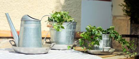 A table with metal watering cans and a pair of glasses, set outdoors with a brick wall and a whiteboard in the background.