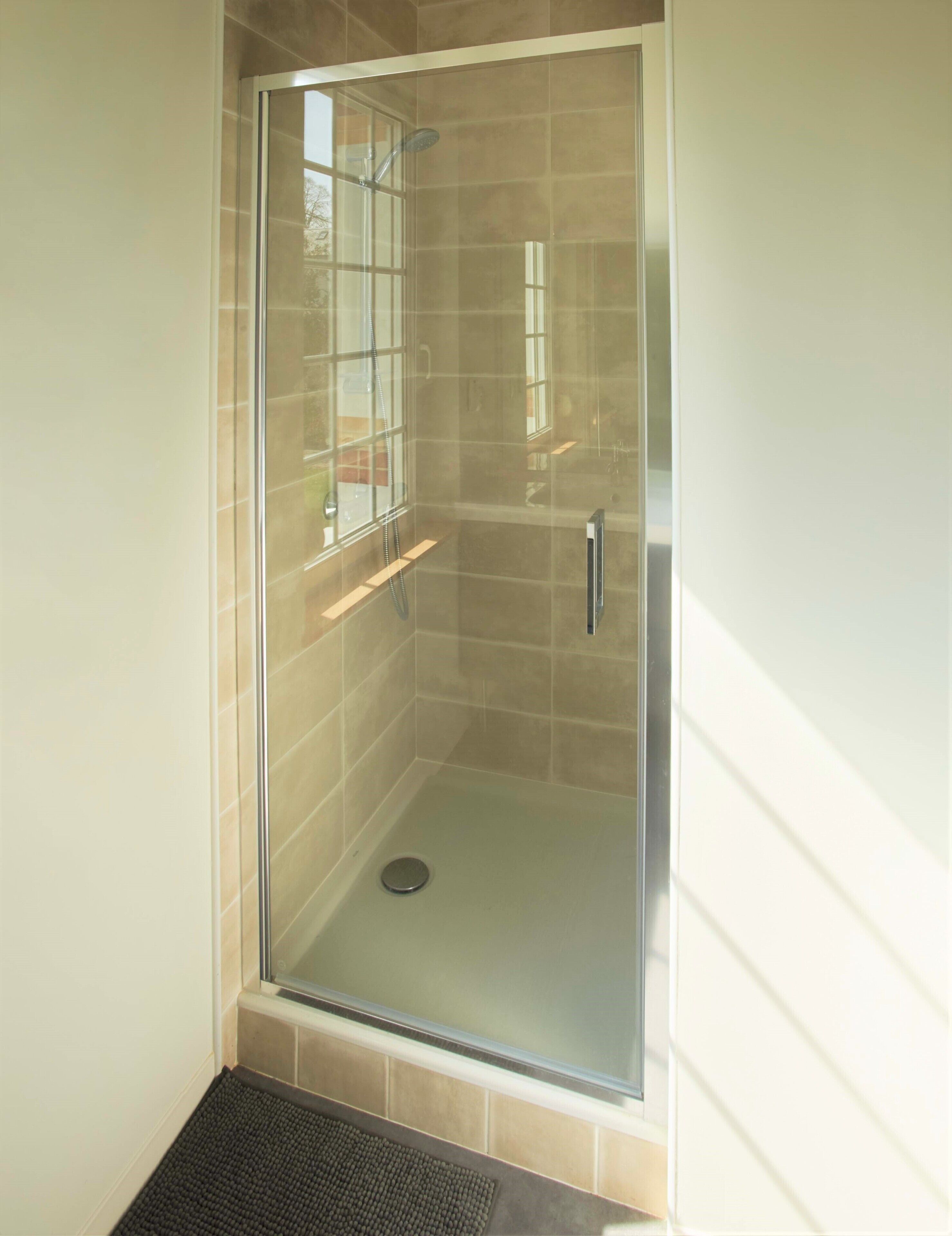 A glass-enclosed shower with a tiled floor and a small shelf.