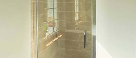 A glass-enclosed shower with a tiled floor and a small shelf.