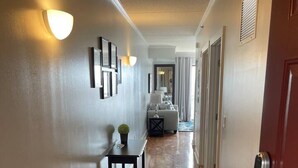 A hallway with a wooden floor, a red door on the right, and a small table with a plant.