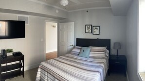 A bedroom with a bed, a ceiling fan, a TV mounted on the wall, a nightstand, and a door.