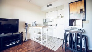 A compact living space with a TV, kitchenette, and artwork on the wall. - Water St. Retreats 03 Historic riverfront paradise (Wilmington)