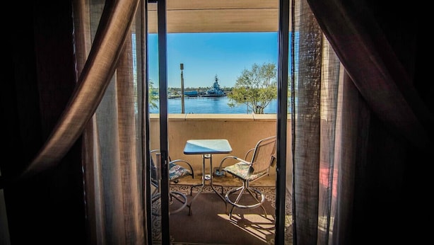 A balcony with a table and two chairs, overlooking a body of water and a distant structure. - Water St. Retreats 03 Historic riverfront paradise (Wilmington)