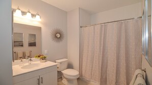 A bathroom with a white sink, mirror, toilet, and shower curtain.