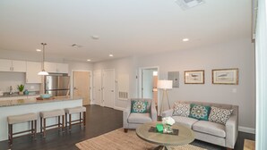 A modern living room with a sofa, coffee table, and a kitchen area with a refrigerator and bar stools.