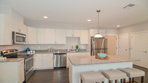 A modern kitchen with white cabinets, stainless steel appliances, and a central island with bar stools.
