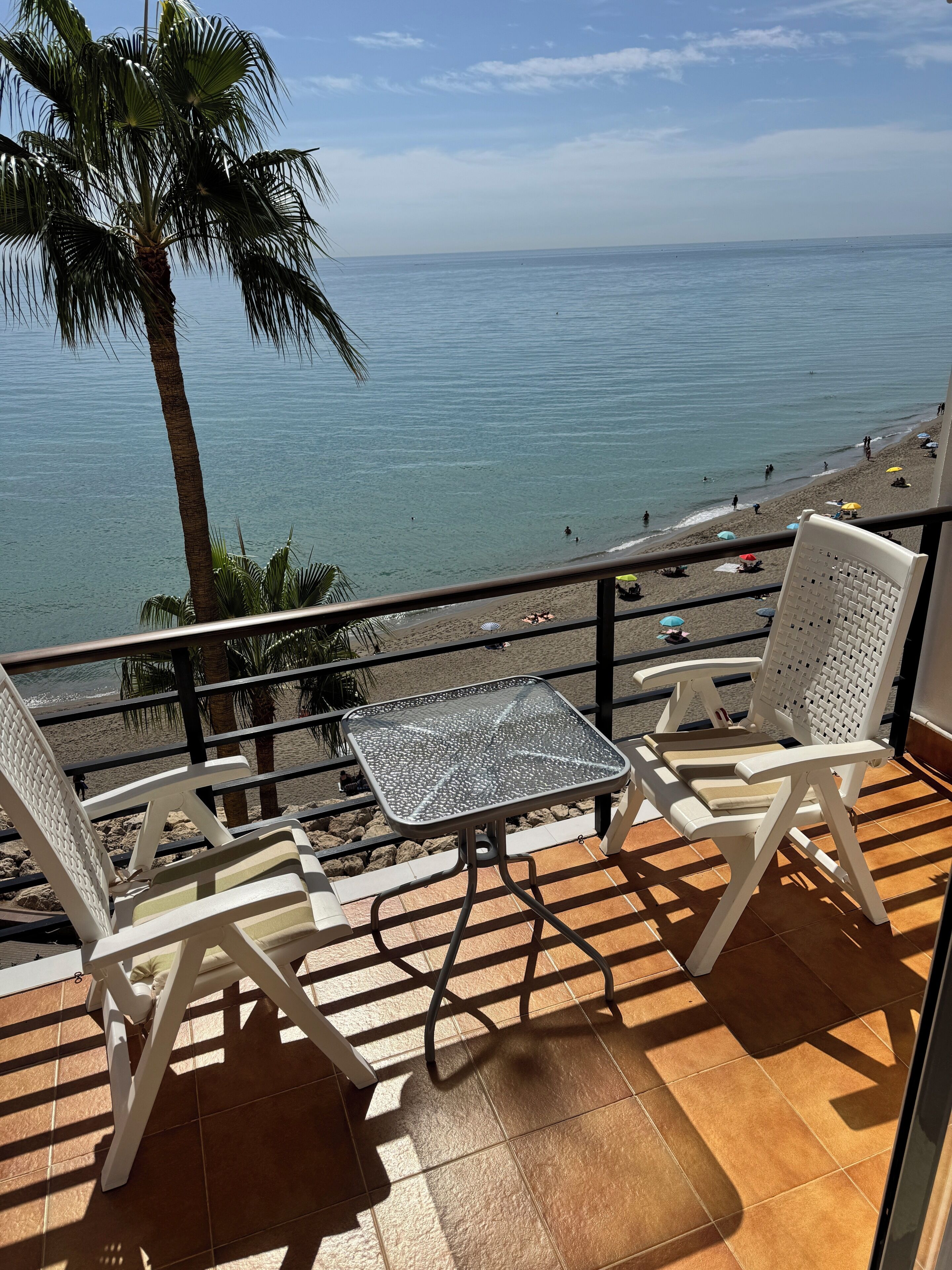 A balcony with two white chairs, a small table, and a view of the beach and ocean.