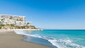 Ein Strandhotel mit mehreren Etagen, einem Sandstrand und klarem, blauem Wasser.