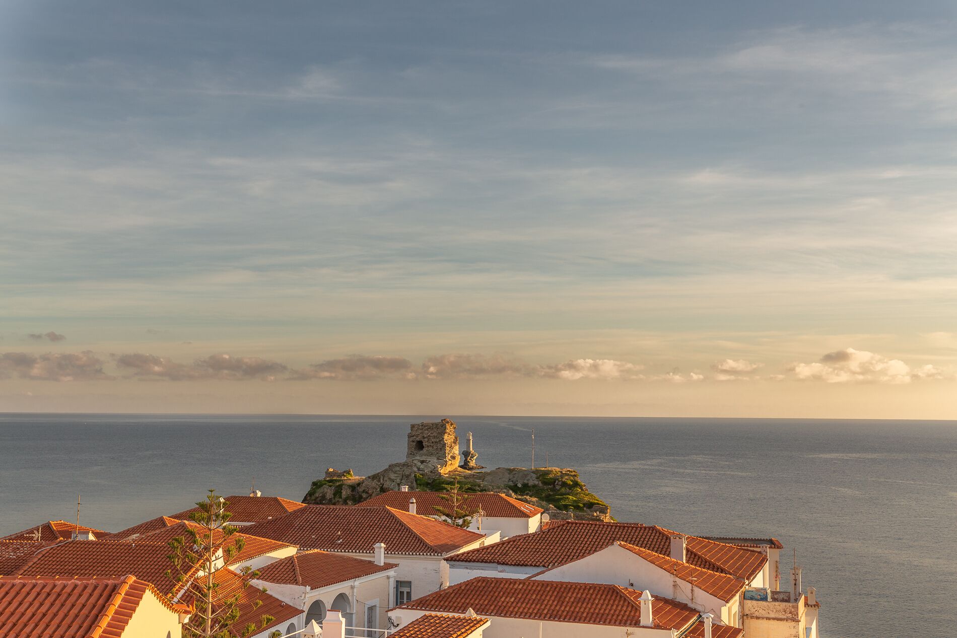 A coastal town with terracotta-roofed buildings, a prominent tower, and a view of the sea.