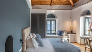A bedroom with a large bed, a desk, and a view of the sea through a window.