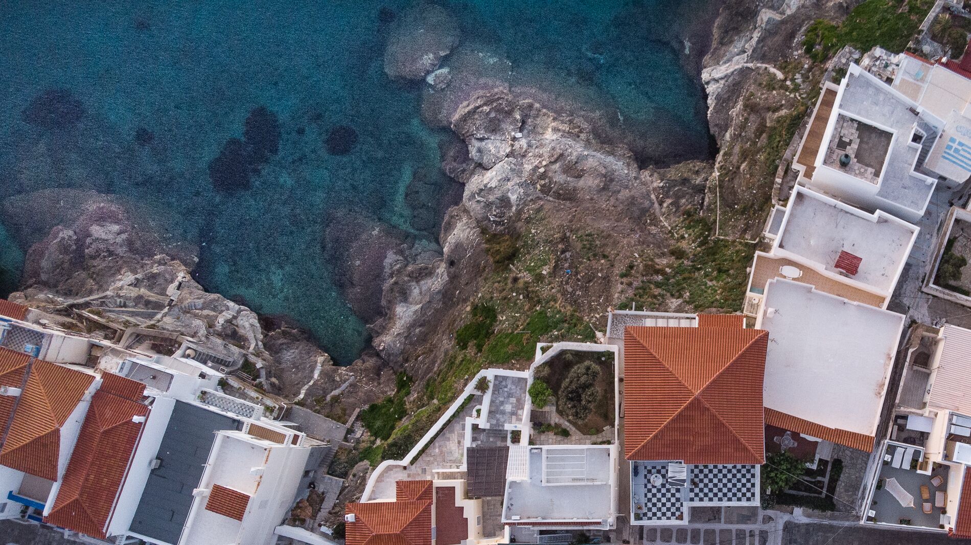 Vista aérea de un pueblo costero con edificios junto a acantilados rocosos y aguas azul turquesa.