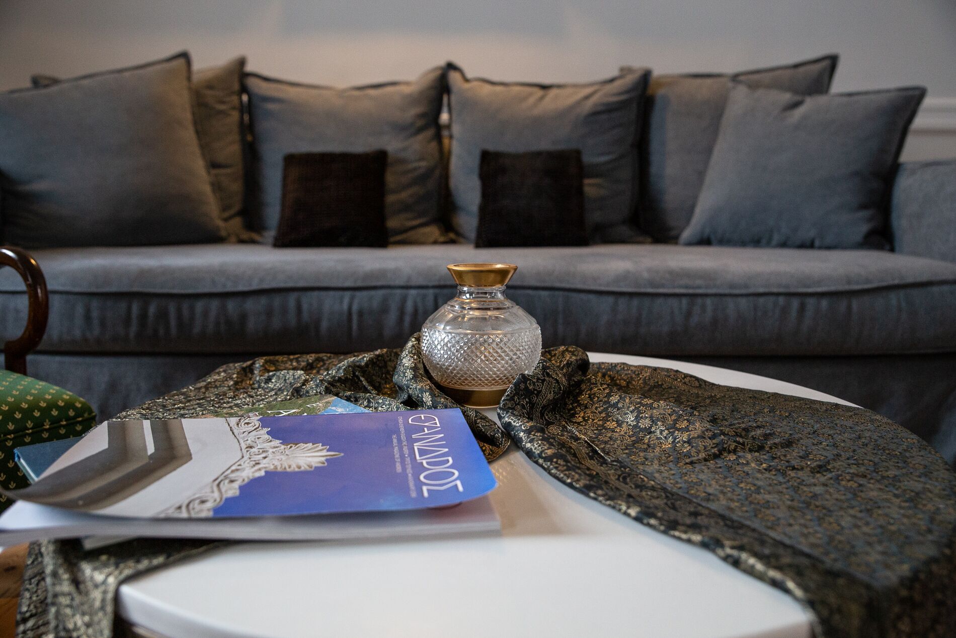 A room with a grey sofa, a patterned throw blanket, a decorative vase, and a magazine on a table.