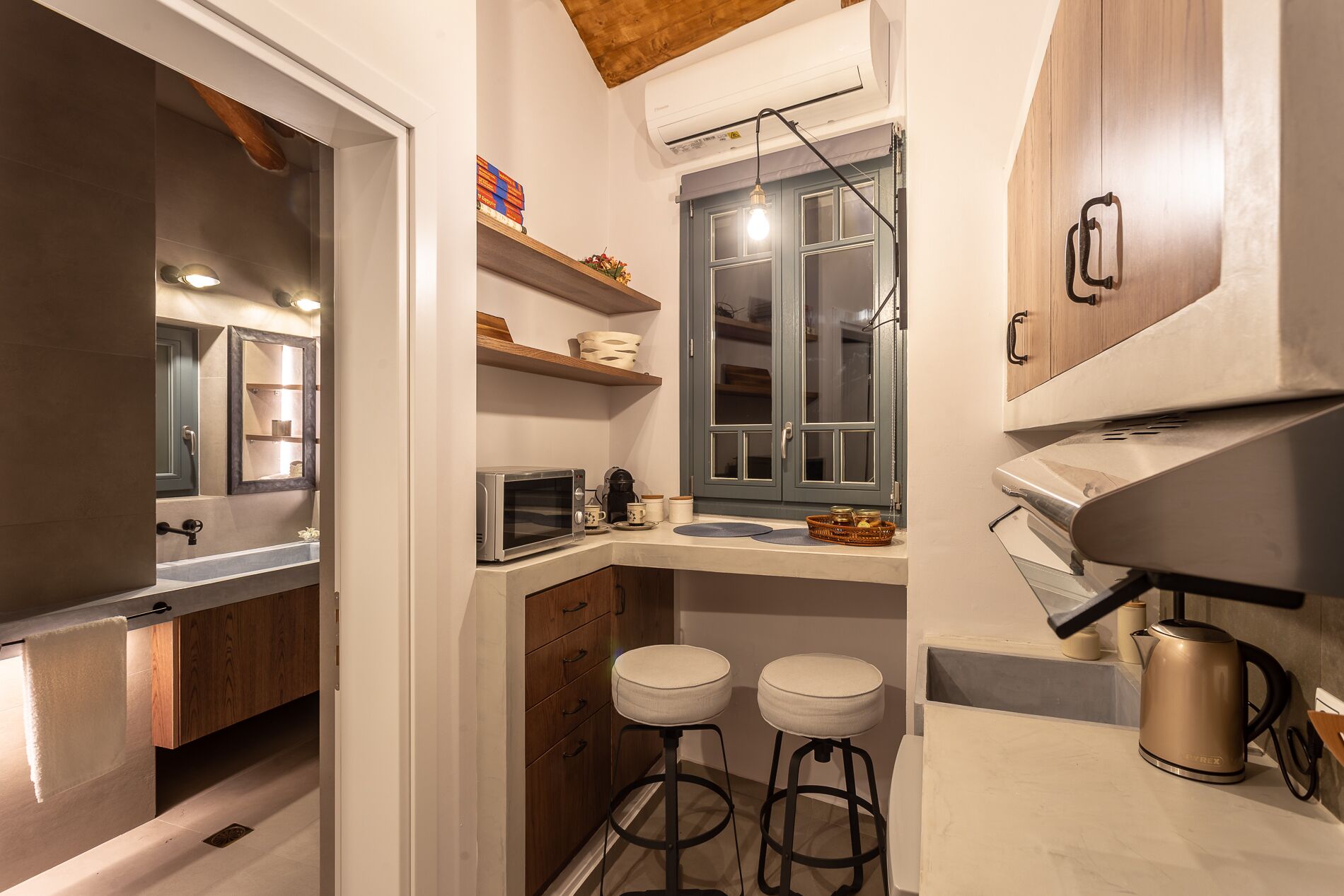 A compact kitchen with a microwave, kettle, and bar stools.