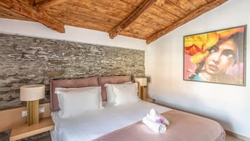 A bedroom with a stone wall, a wooden ceiling, a bed with white bedding, and a painting on the wall.