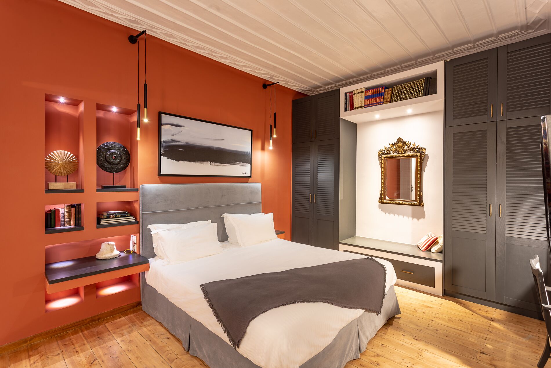 Une chambre à coucher moderne avec un grand lit, des étagères intégrées remplies de livres, un tableau abstrait encadré et un miroir décoratif.