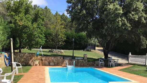 A rectangular swimming pool with a stone border, surrounded by a grassy area with a few chairs and tables. - El Magnolio Rural Cottage (Santa Cruz de Pinares, Ávila)