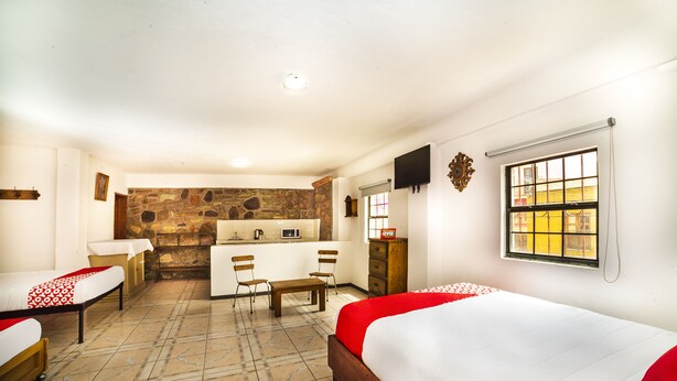 Une chambre d’hôtel avec deux lits, une kitchenette, un mur en pierre, une télévision et une fenêtre donnant sur un beau paysage.